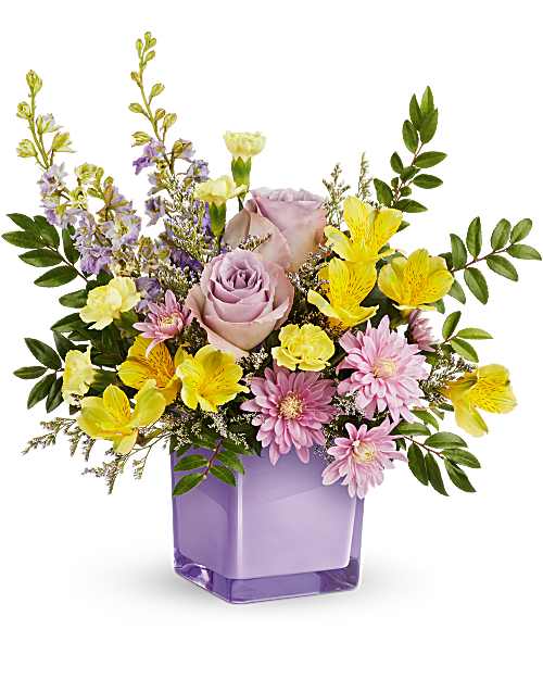 Pastel Paradise Bouquet  - Bring a soft touch of spring indoors with a Pastel Paradise Bouquet. Lavender roses and golden blooms shine in a radiant purple glass cube, creating a fresh, joyful display of color and beauty. The Pastel Paradise Bouquet features lavender roses, yellow alstroemeria, yellow miniature carnations, lavender larkspur, lavender cushion spray chrysanthemums, and white limonium, accented with lush huckleberry. Designed in an amethyst-colored glass cube vase. This arrangement is a small to medium size arrangement. 