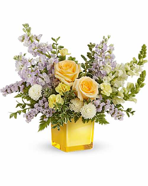 Sunshine Dreams Bouquet  - Bright and serene, Sunshine Dreams Bouquet blends soft yellow roses and cheerful white blooms with hints of lavender, creating a radiant display of happiness in a glowing yellow glass cube. The Sunshine Dreams Bouquet features yellow roses, yellow miniature carnations, lavender stock, white button spray chrysanthemums, white snapdragons, and lavender statice, accented with leatherleaf fern and oregonia. Arranged in a yellow glass cube vase. * *This Arrangement is a small to medium size**