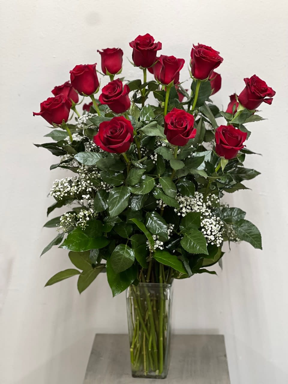 Red roses arranged in a clear glass vase with white filler flowers.