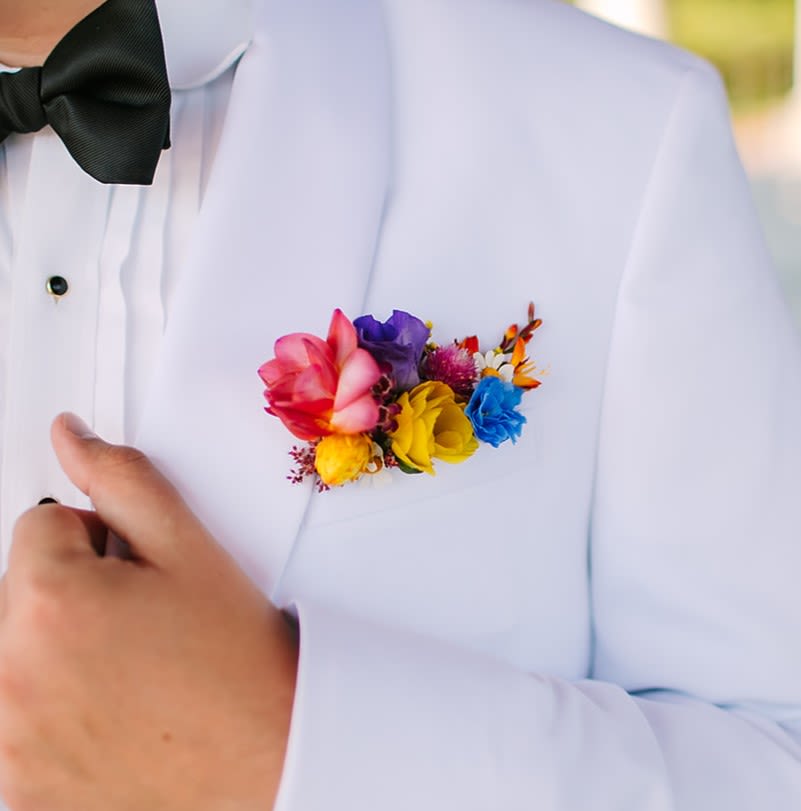 Bright multicolor pocket flower arrangement on a white tuxedo jacket with a black bow tie.