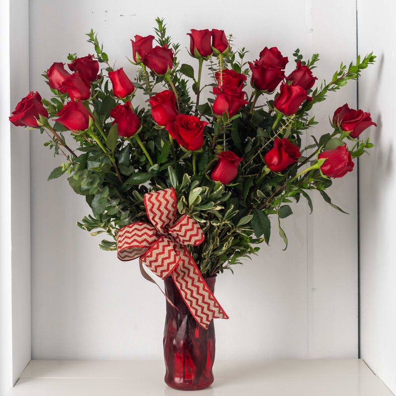 Tall arrangement of long-stem red roses in a red glass vase with chevron ribbon bow