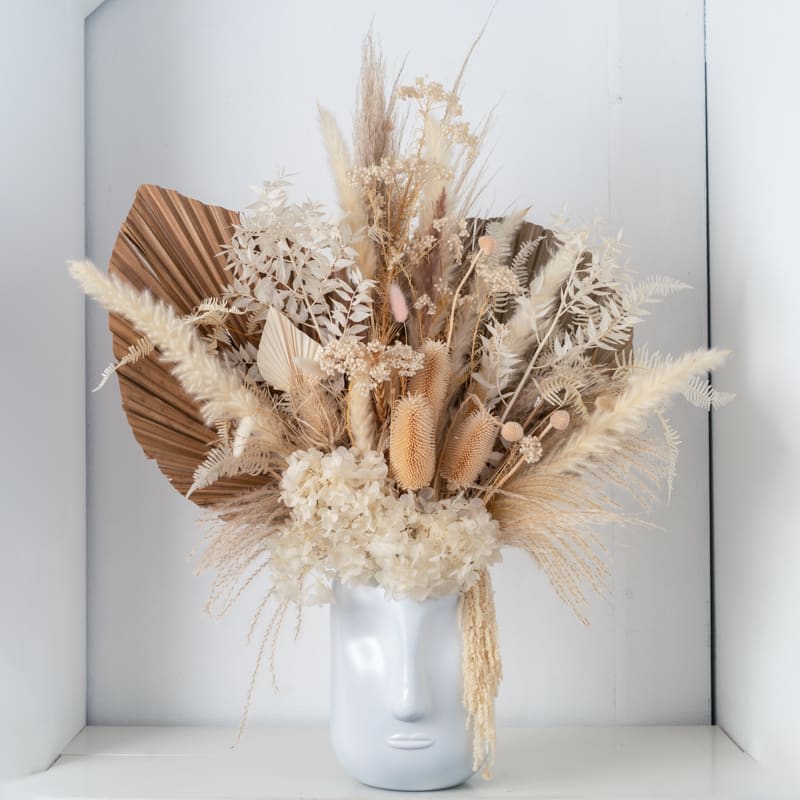 Neutral dried flower arrangement with hydrangea and grasses in a white ceramic face-shaped vase