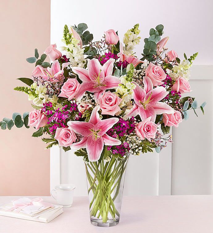 Tall mixed arrangement of pink lilies and roses with white flowers in a clear glass vase