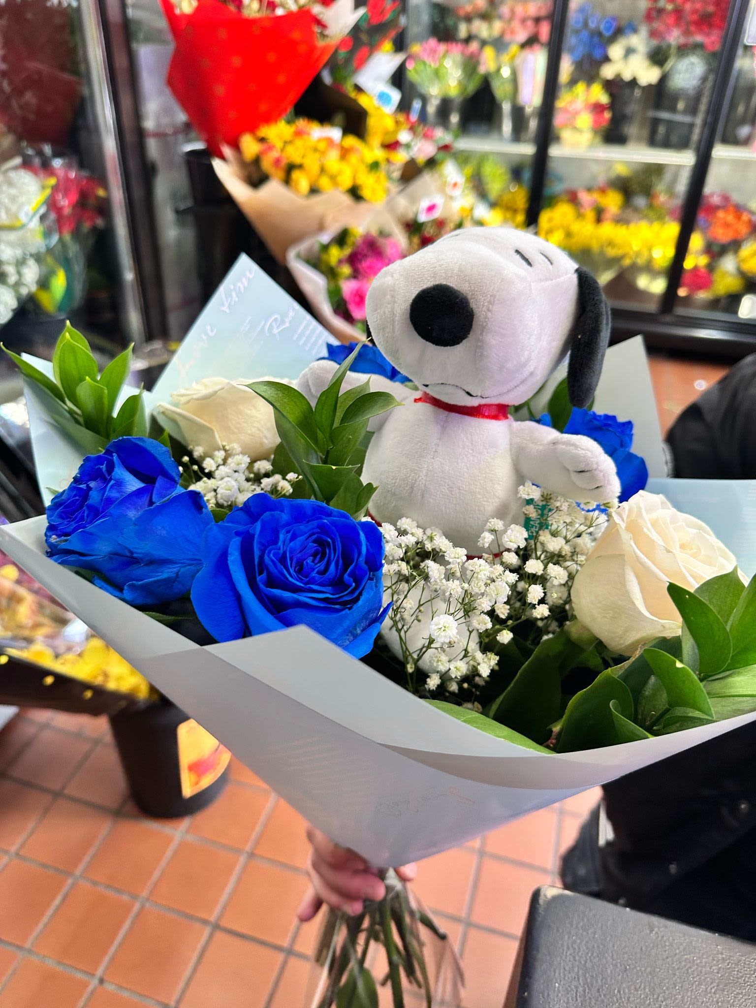 Bouquet of blue and white roses with baby's breath and a Snoopy plush toy wrapped in light paper