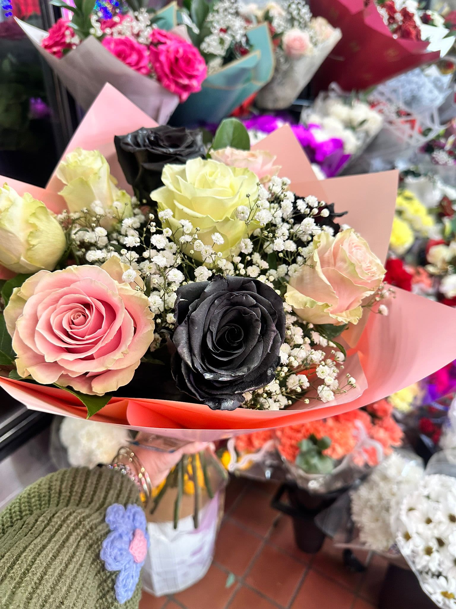 Hand-tied bouquet of pink, cream, and black roses with white filler flowers in pink wrap