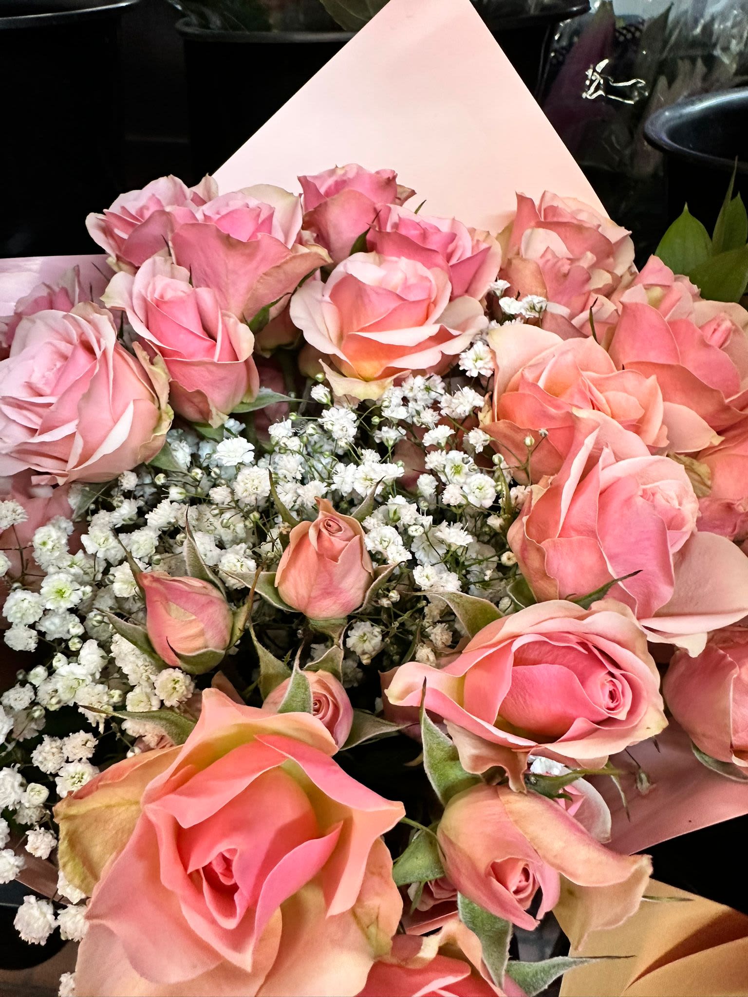 Hand-tied bouquet of pink roses with white filler flowers wrapped in soft pink paper