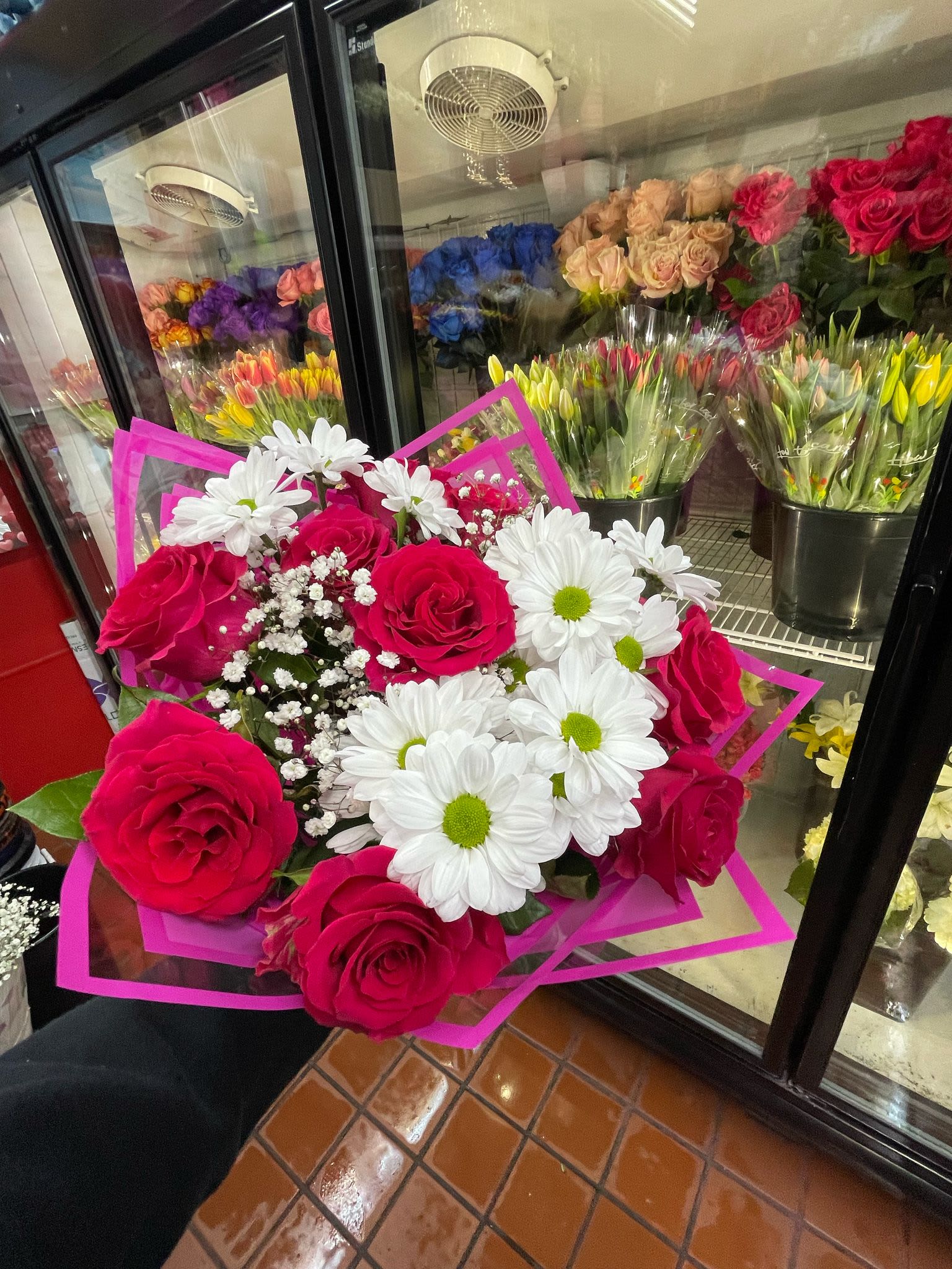 Hand-tied bouquet of hot pink roses, white daisies, and baby's breath in bright pink wrap