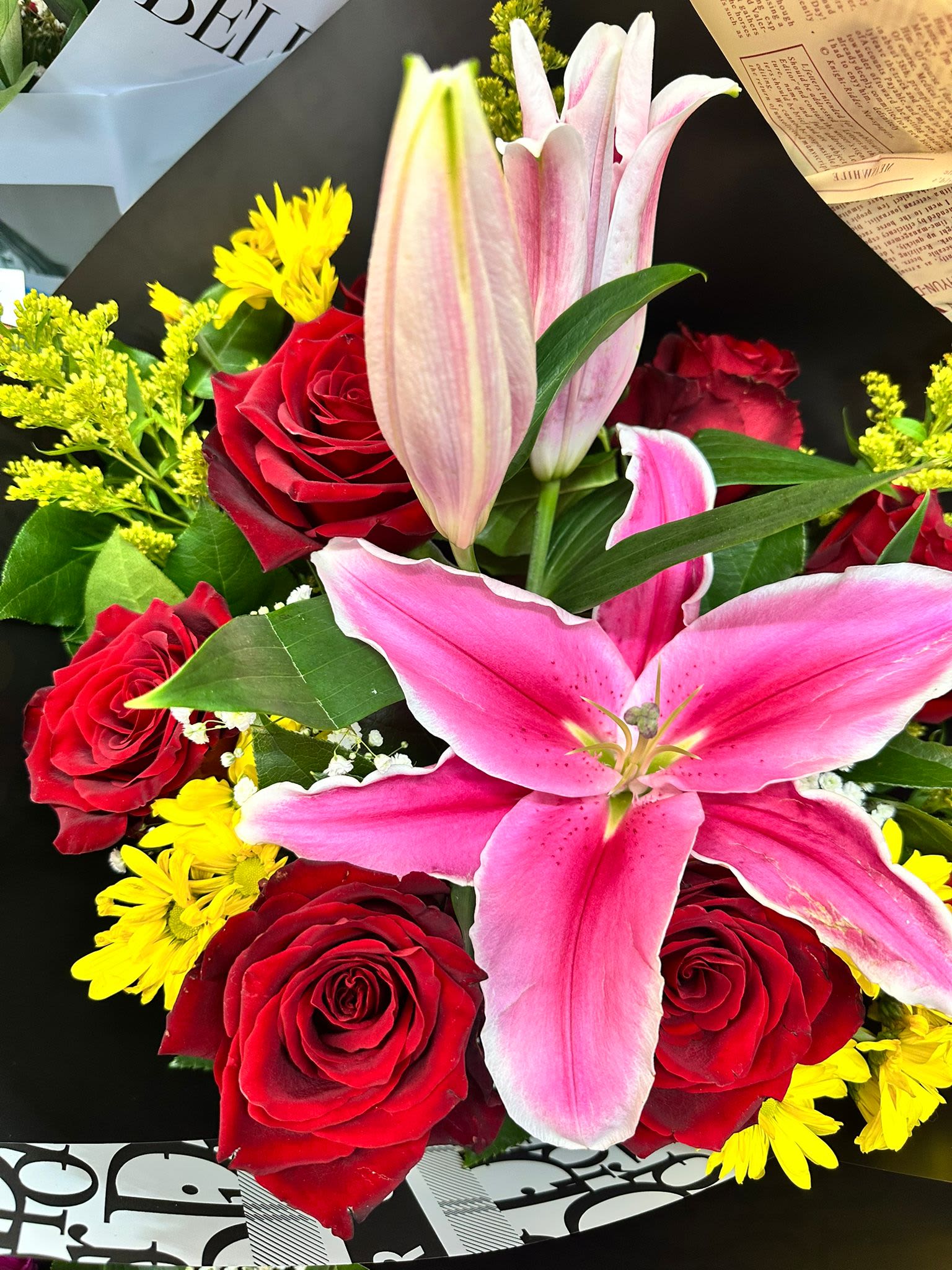 Bouquet of pink lilies, red roses, and yellow daisies wrapped in black and white paper