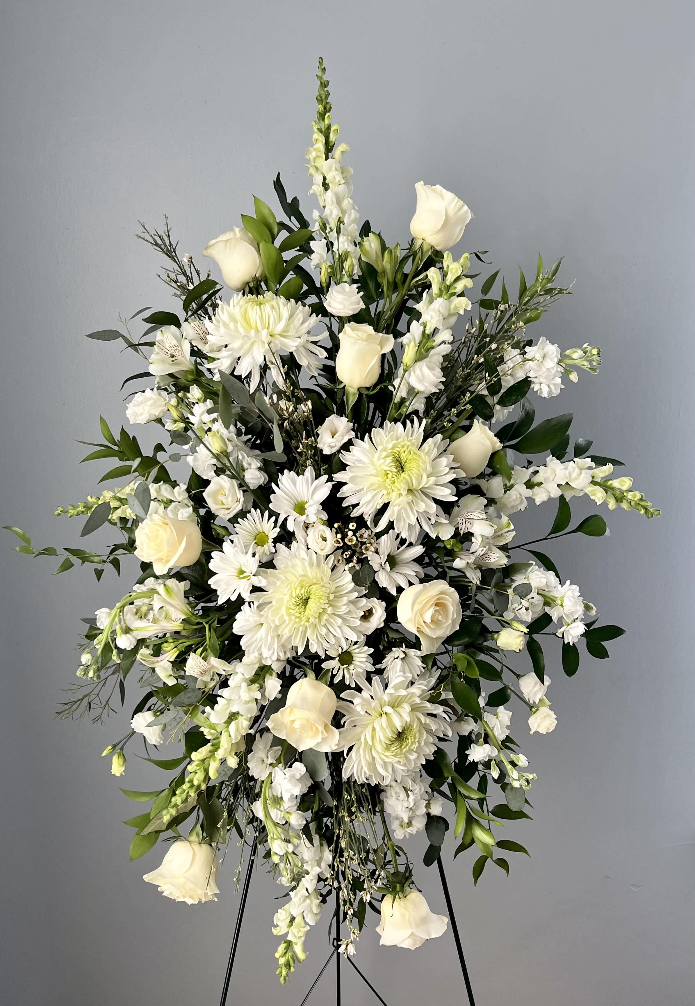 Tall standing spray of white roses, daisies, and snapdragons on a metal easel.