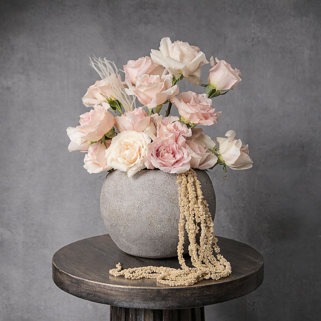 Low arrangement of blush and ivory roses in a round gray vase with cascading dried accents.