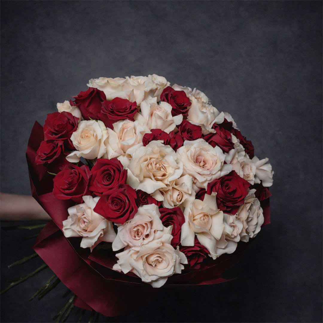 Large round bouquet of red and cream roses wrapped in deep red paper