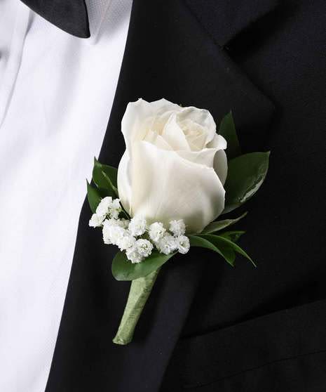 White rose boutonniere with small white filler flowers pinned to a black suit lapel