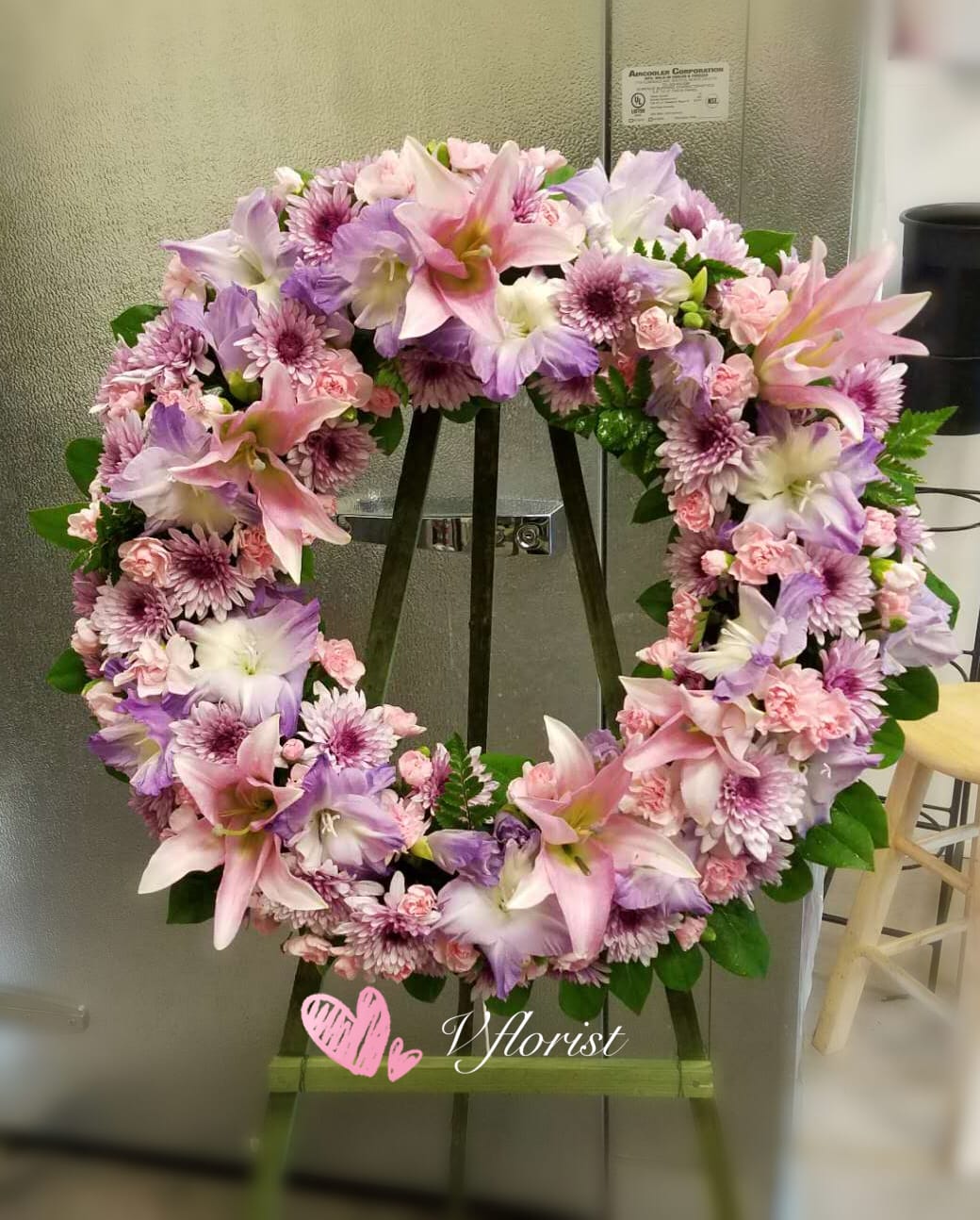 Pink and lavender wreath of lilies, carnations, and mums displayed on a wooden easel