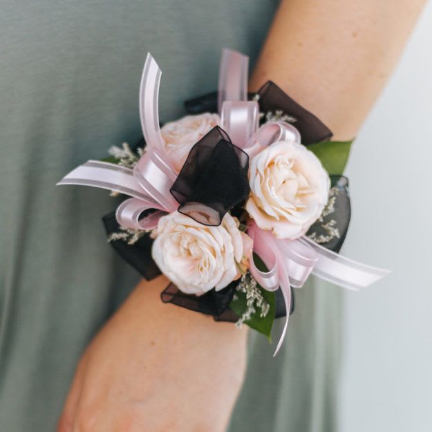 Blush rose wrist corsage with pink and black ribbon on a person’s arm