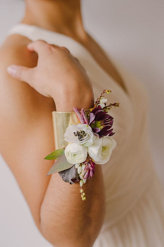 Gold cuff bracelet corsage with white and plum flowers worn on a person's forearm