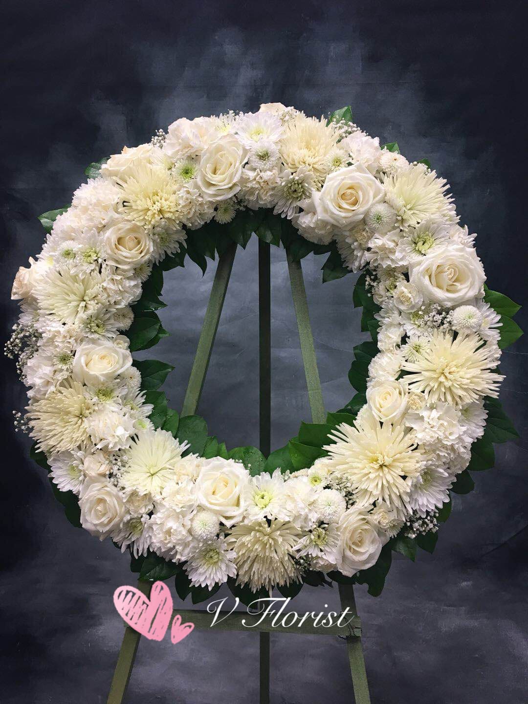Large white rose and chrysanthemum wreath on a stand against a dark background
