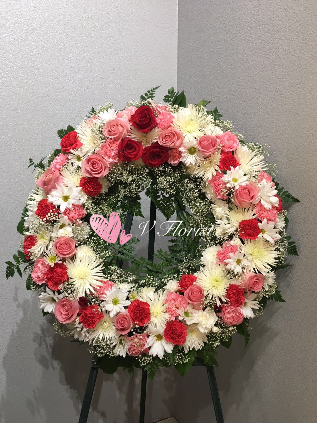 Standing wreath with pink and red roses, carnations, and white daisies on an easel