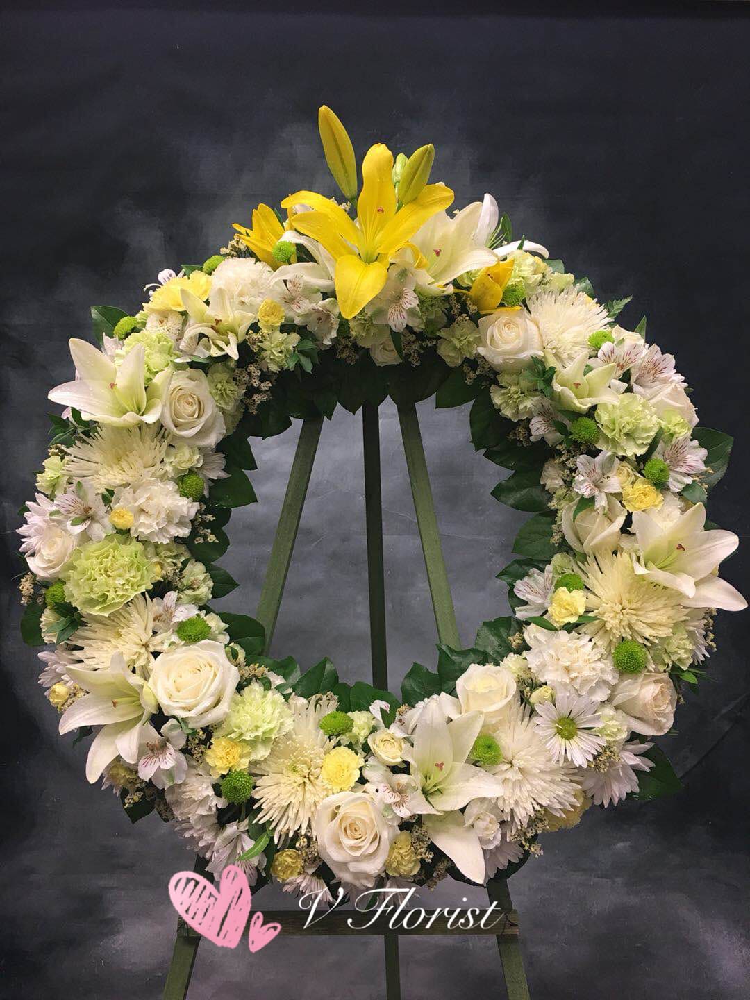 Standing wreath of white and yellow lilies, roses, and mums on a green easel