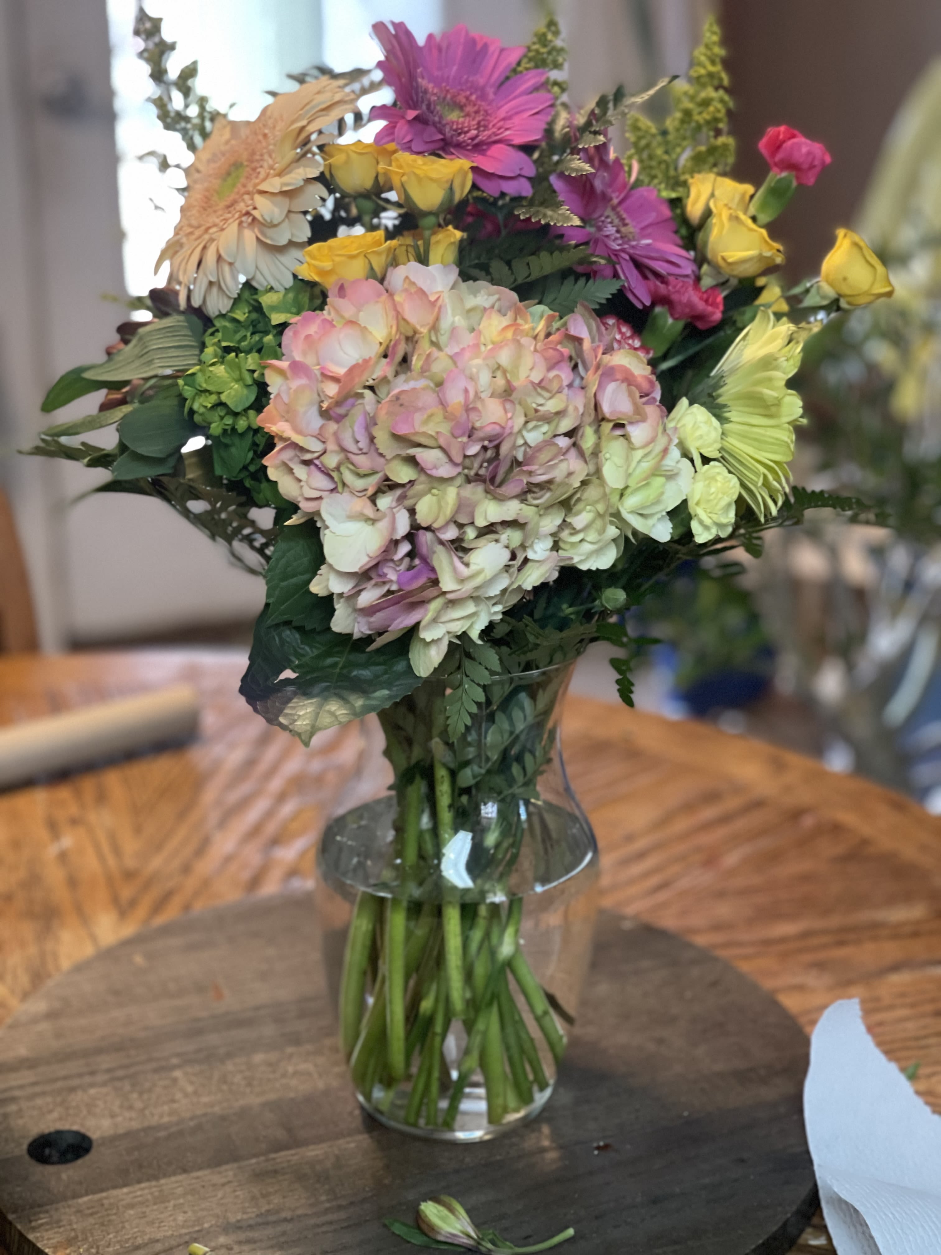 Mixed bouquet with hydrangea, gerbera daisies, and yellow roses in a clear glass vase