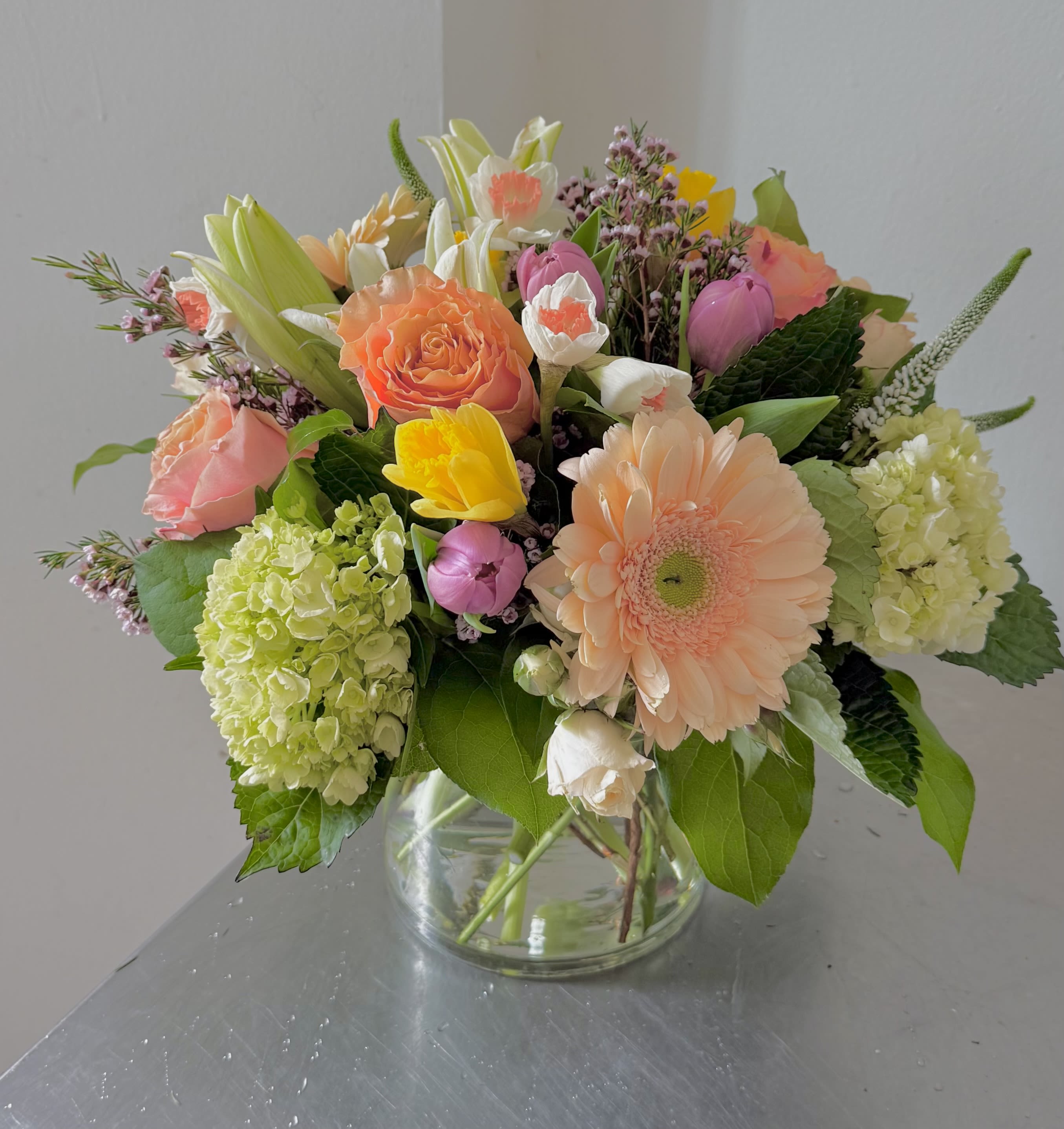 Simply Spring - Bring the fresh, vibrant energy of a new season indoors with our stunning Simply Spring arrangement. This abundant, handcrafted bouquet is a beautiful blend of pastel and bright hues, expertly designed to capture the essence of a blooming garden.   Presented in a classic clear glass vase, this arrangement features a delightful assortment of seasonal flowers:     