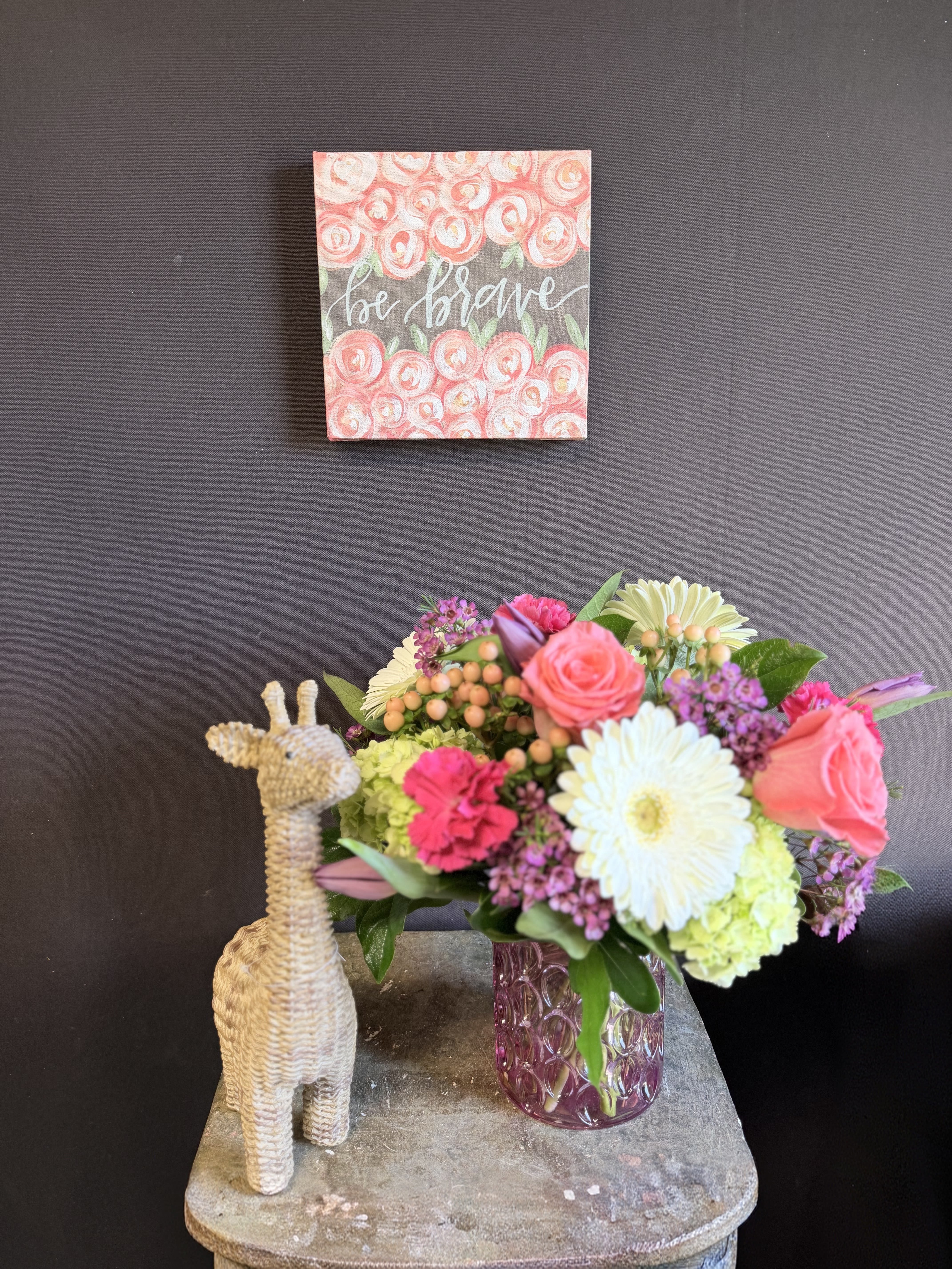Be Brave Blooming Giraffe Bouquet Trio  - Bright, joyful, and full of encouragement, our Be Brave Blooming Giraffe Bouquet is the perfect way to send a cheerful lift. A mix of brightly colored fresh flowers—mini green hydrangea, roses, tulips, waxflower, Hypericum berries, and Gerbera daisies—are artfully arranged with lush greenery in a charming pink glass vase.  This spirited arrangement is paired with a sweet wicker giraffe accent and a pink floral-pattern square canvas sign that reads “be brave”—a heartfelt reminder of strength and courage. Ideal for birthdays, get well wishes, new beginnings, or any moment that calls for a little extra bravery and a lot of color.