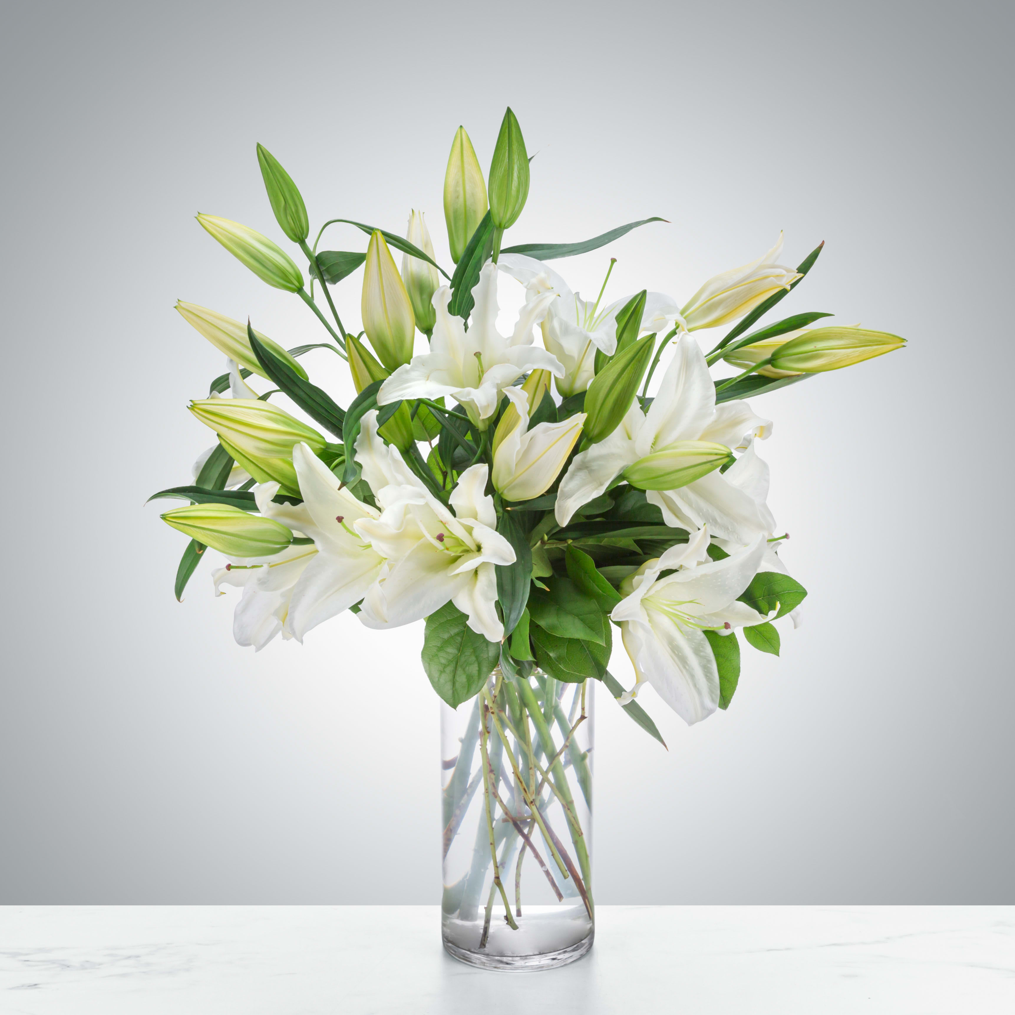 Tall arrangement of white lilies with buds in a clear glass vase
