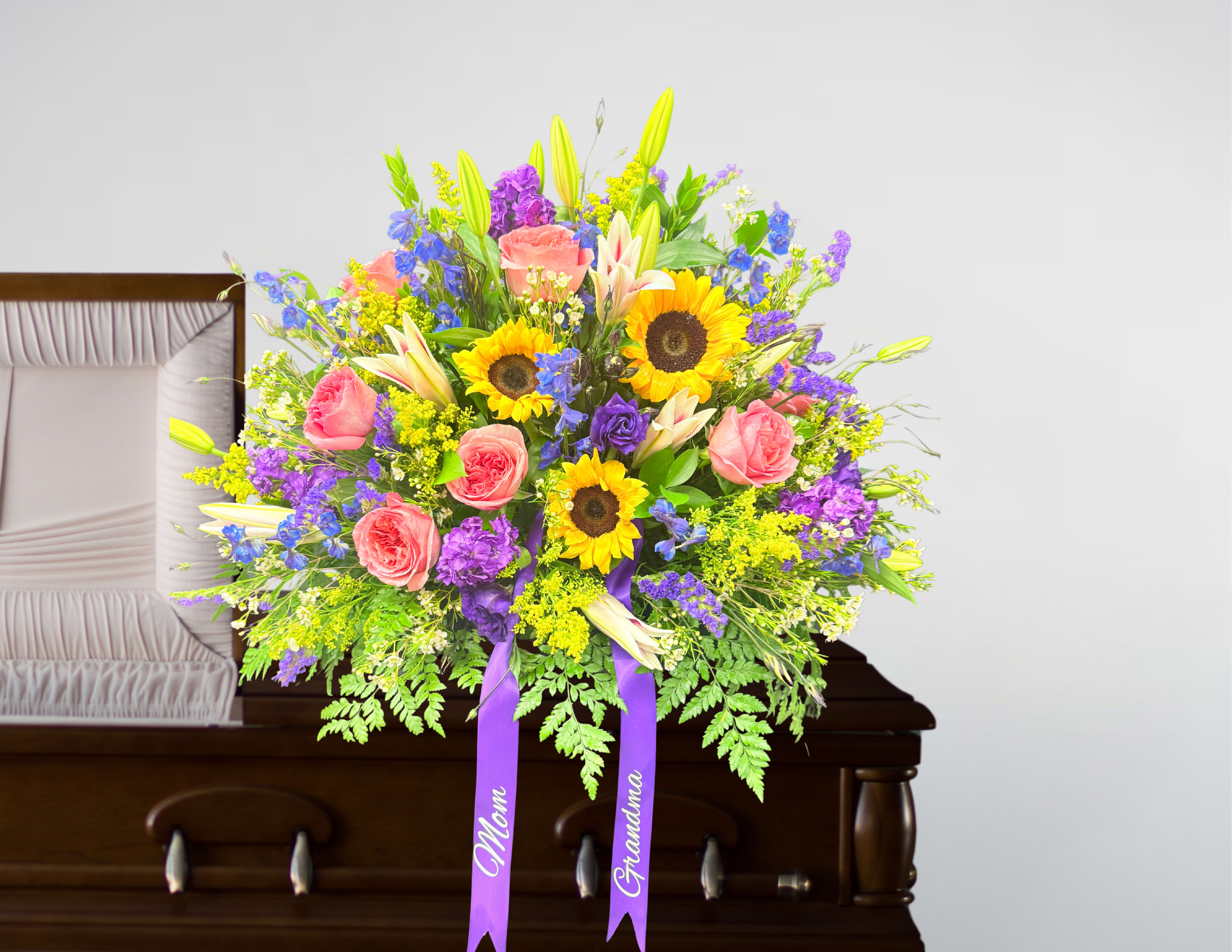 Bright casket spray with sunflowers, pink roses, lilies and purple blooms on a wooden casket