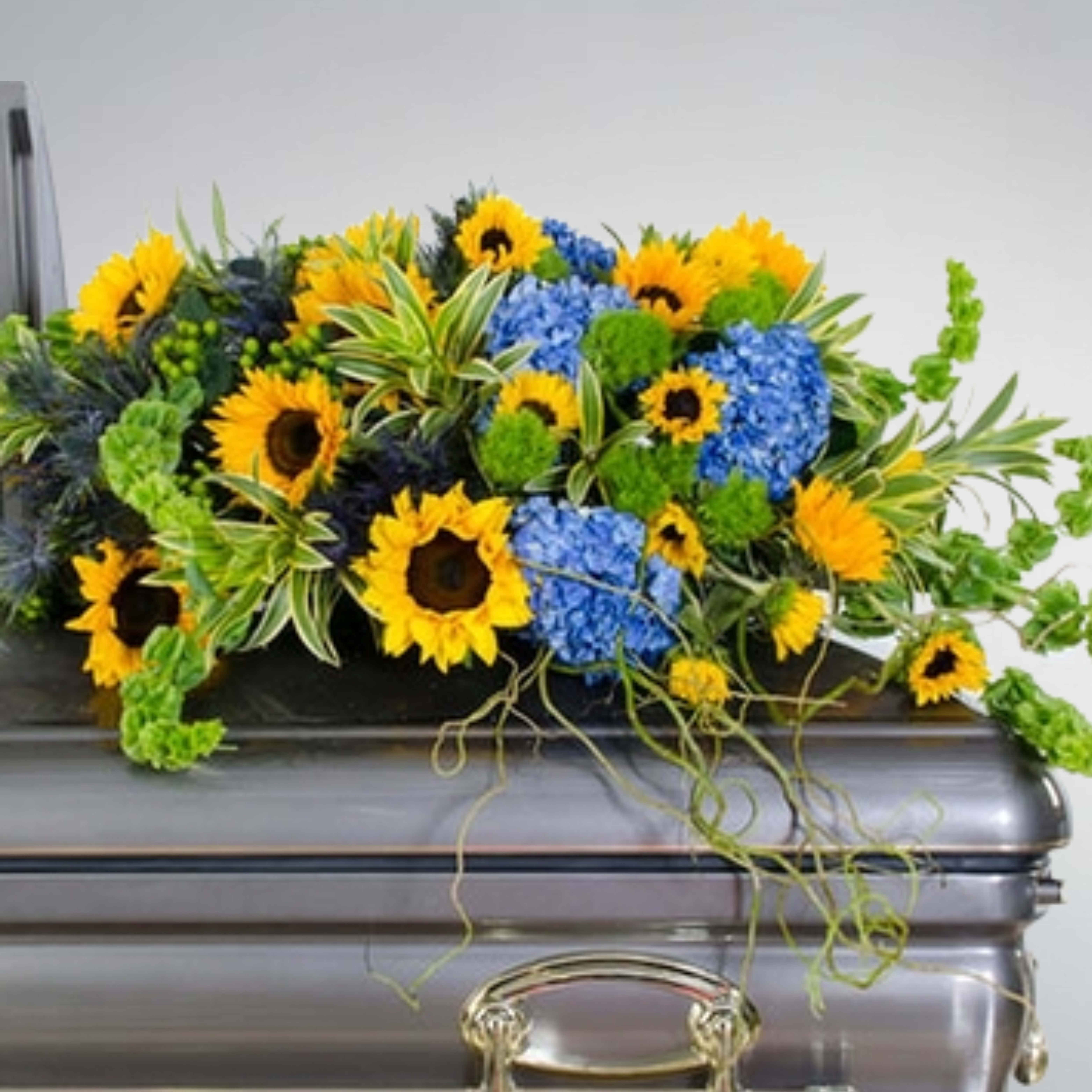 Casket spray of yellow sunflowers and blue hydrangeas with green accents on a silver casket