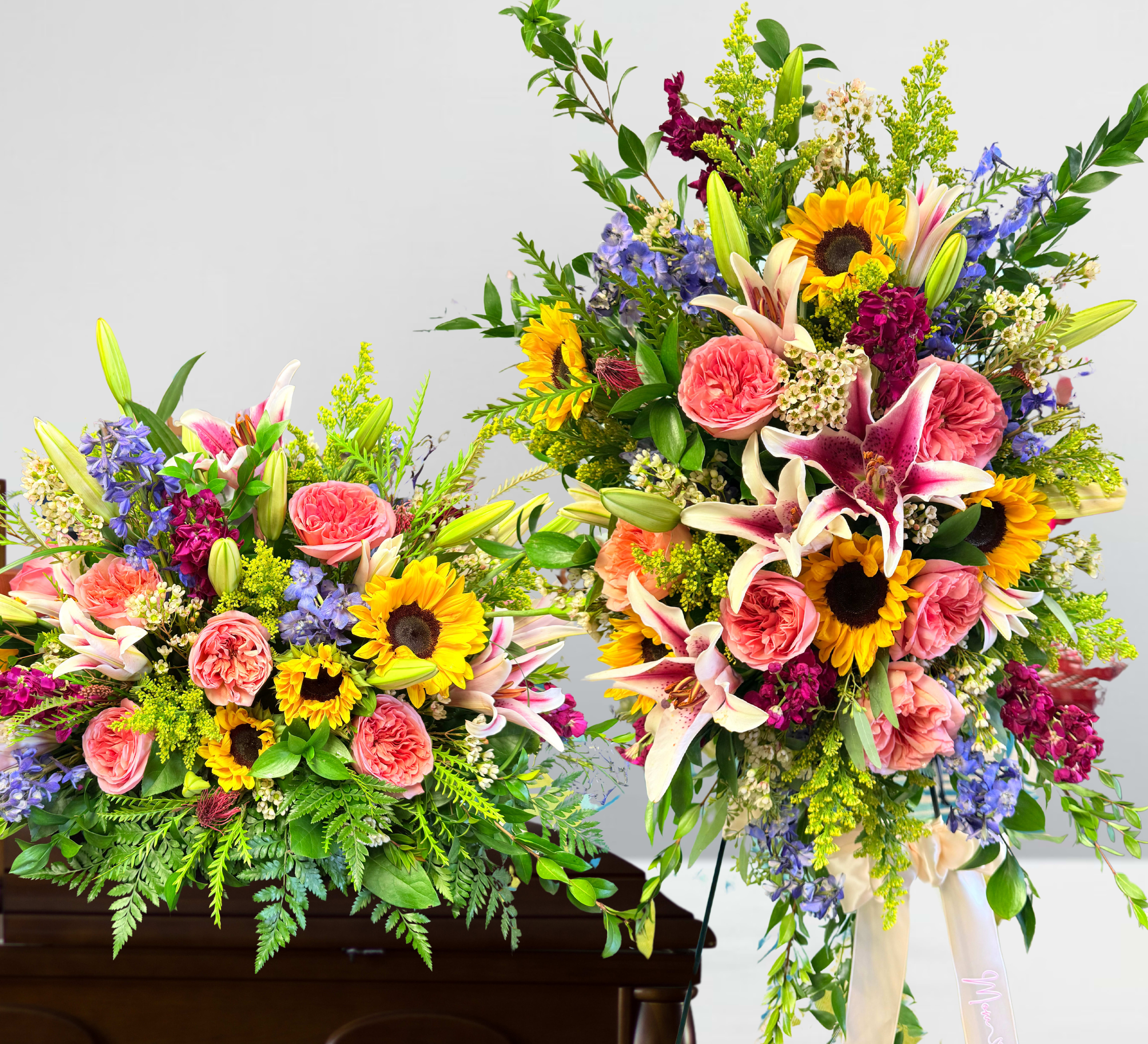 Colorful sunflower, lily, and rose sympathy sprays on a wooden casket and standing easel