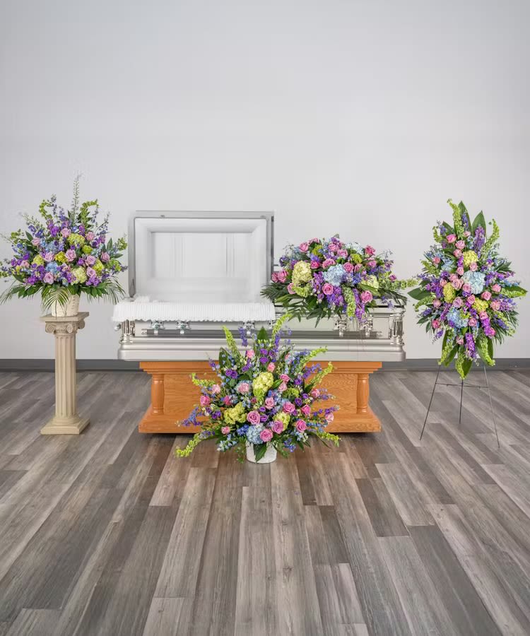 Set of pastel funeral flower arrangements surrounding an open casket in a chapel.