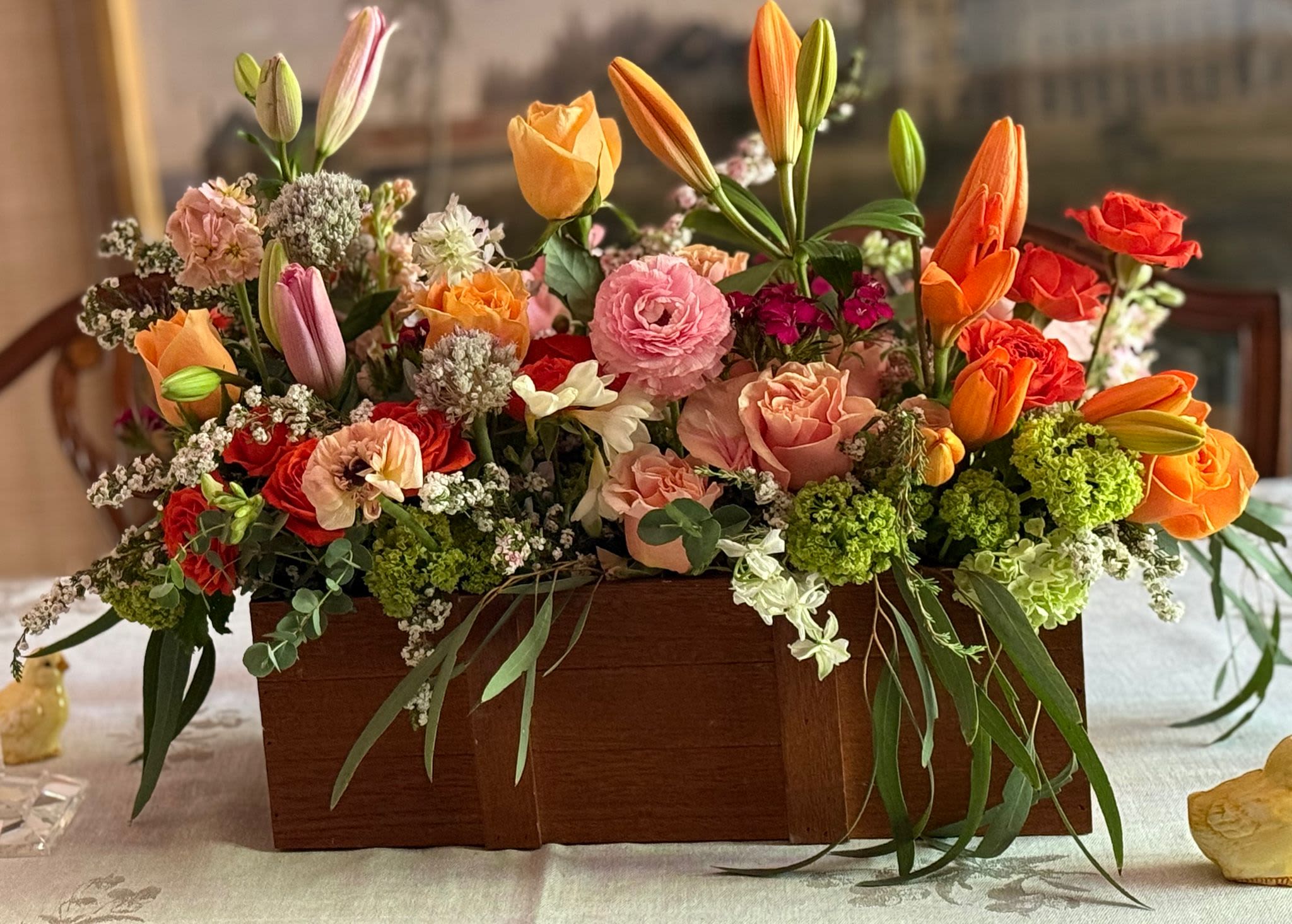 Rectangular wooden box filled with orange tulips, pink and peach roses, and mixed spring flowers