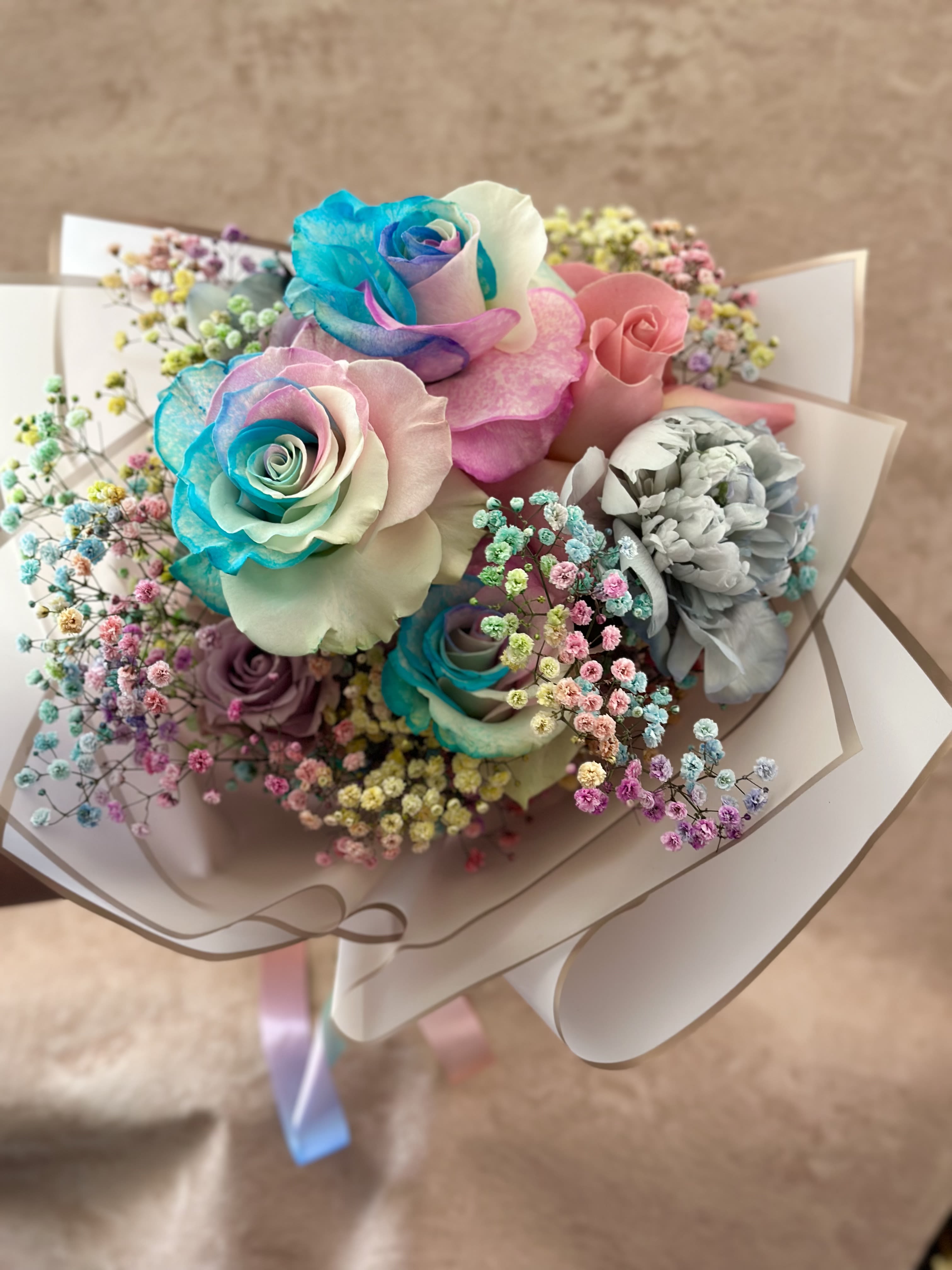 Bouquet of pastel rainbow roses with colorful baby's breath wrapped in white paper