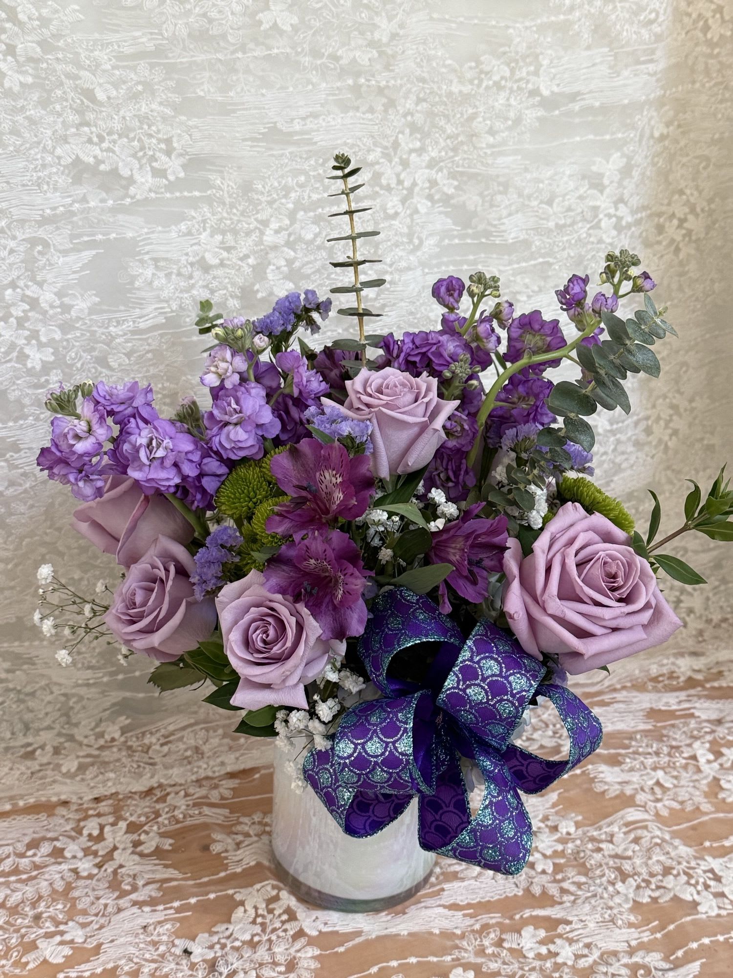 Mermaid Garden - Arrangement is filled with lavender roses, lavender stock, purple alstroemeria, green mums, eucalyptus and seasonal greens tied together with a mermaid bow. 