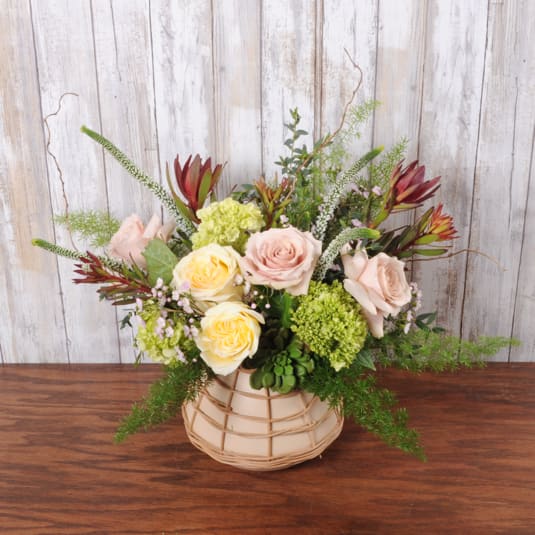 Low peach and yellow rose arrangement with green accents in a round basket vase