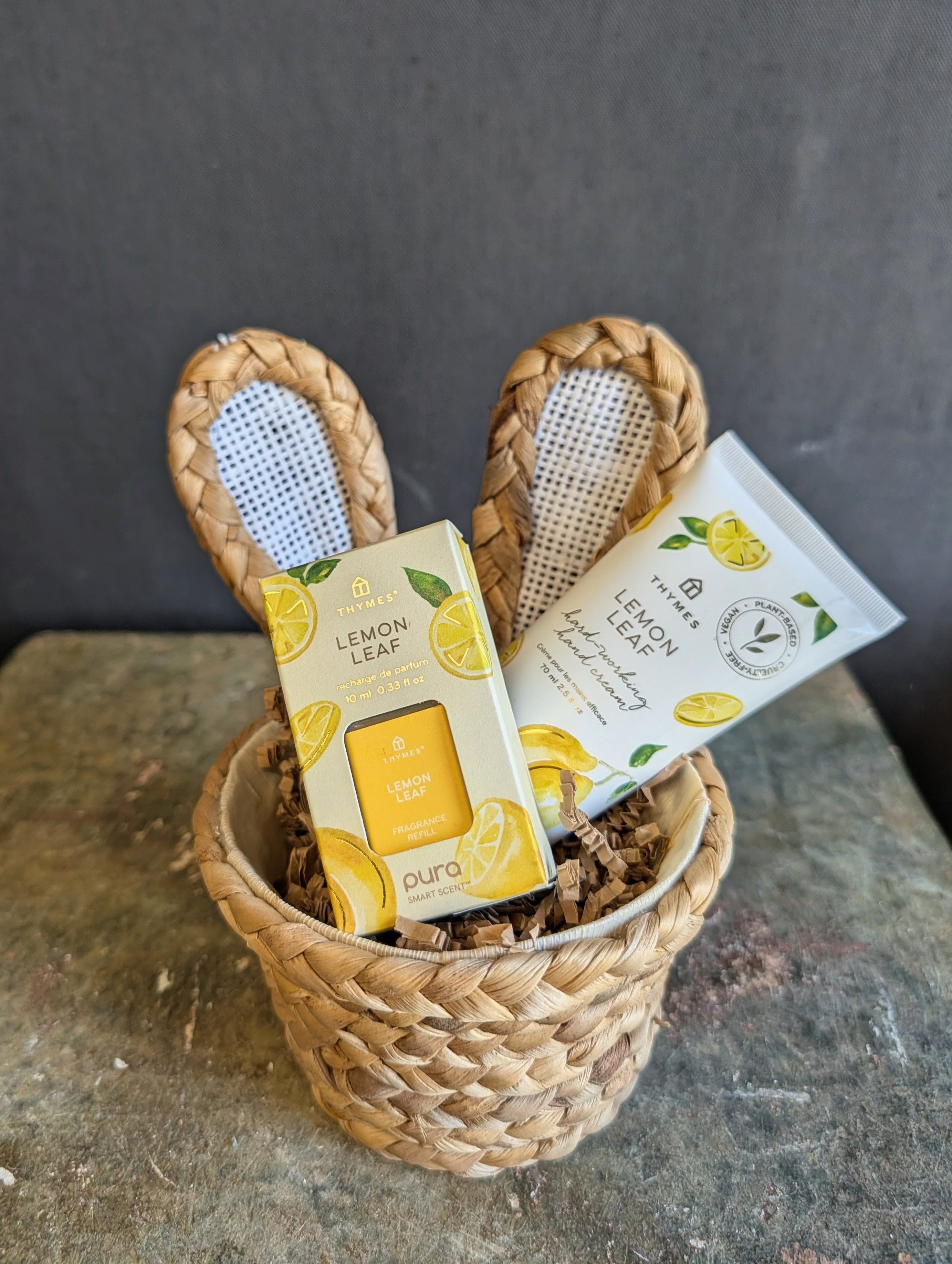 SALE Bunny Lemon Leaf Pampering Basket - A petite wicker basket topped with sweet bunny ears, filled with fresh, uplifting Lemon Leaf favorites from Thymes. Inside, you’ll find a Pura smart fragrance refill in crisp Lemon Leaf to scent your home, plus a 2.5 oz Lemon Leaf Hard-Working Hand Cream that softens and nourishes skin with a bright, clean citrus aroma—perfect for tucking into a gift basket or gifting on its own.