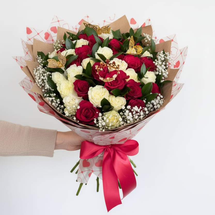 Hand-tied bouquet of red and cream roses with baby's breath wrapped in heart paper and red ribbon