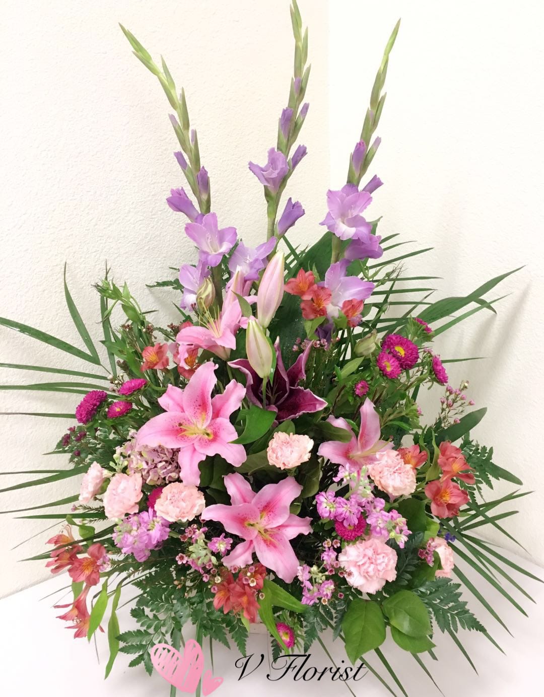 Tall pink and purple mixed flower arrangement with lilies and carnations in a fan-shaped design