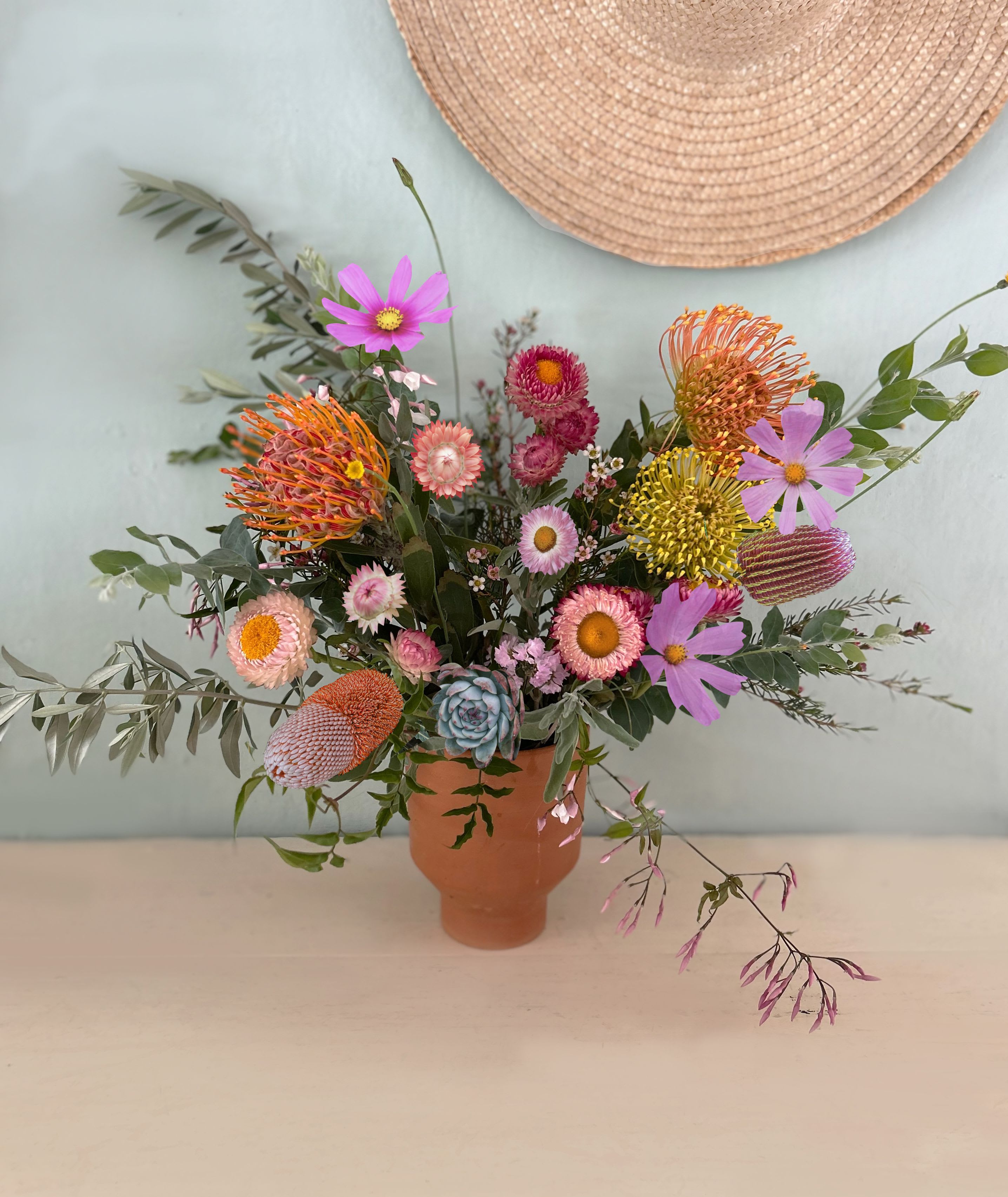 The Wild Desert - A large and lovely, natural and wild arrangement in the colors of LA's nature. Strawflowers, pincushion proteas, banksia flower, cosmos, wax flowers, olive, eucalyptus, lavender, jasmin and succulents adorn the timeless and elegant arrangement placed in a clay vase and ready for hand delivery in LA by our own delivery staff.