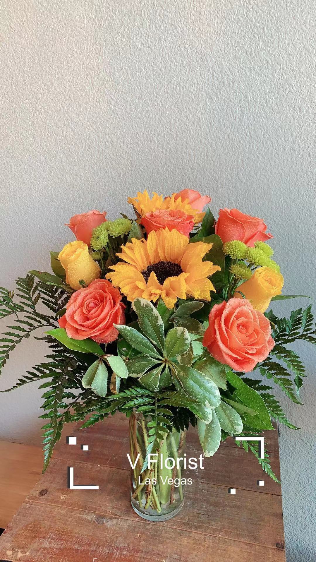 Vase arrangement with orange roses, yellow sunflower and yellow roses with green accents