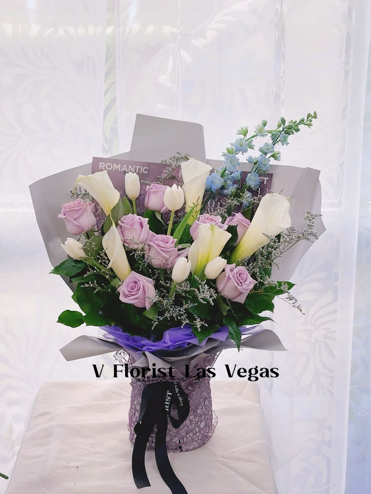 Arrangement of lavender roses, white tulips, and calla lilies in wrapped bouquet with purple accents