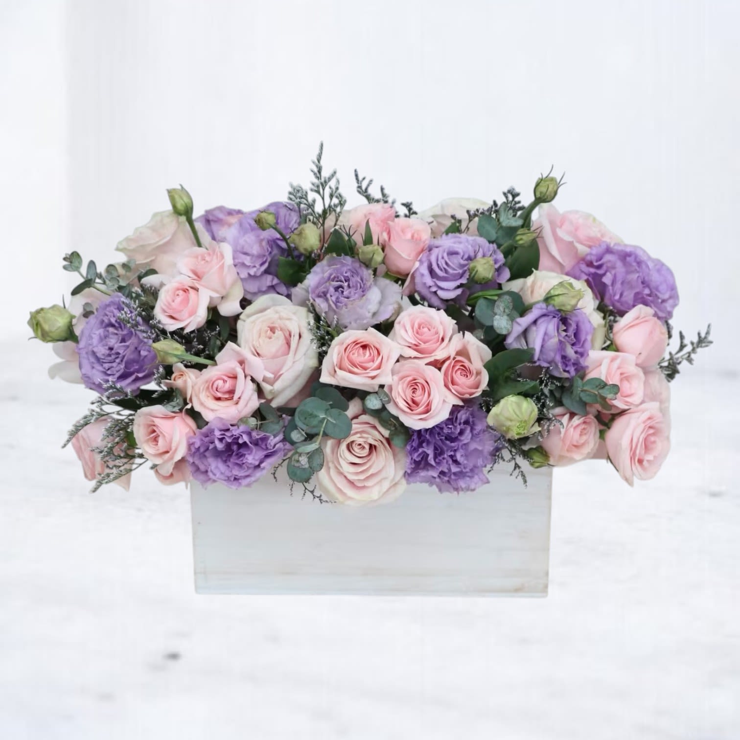 Low arrangement of pink roses and lavender lisianthus in a white rectangular wooden box