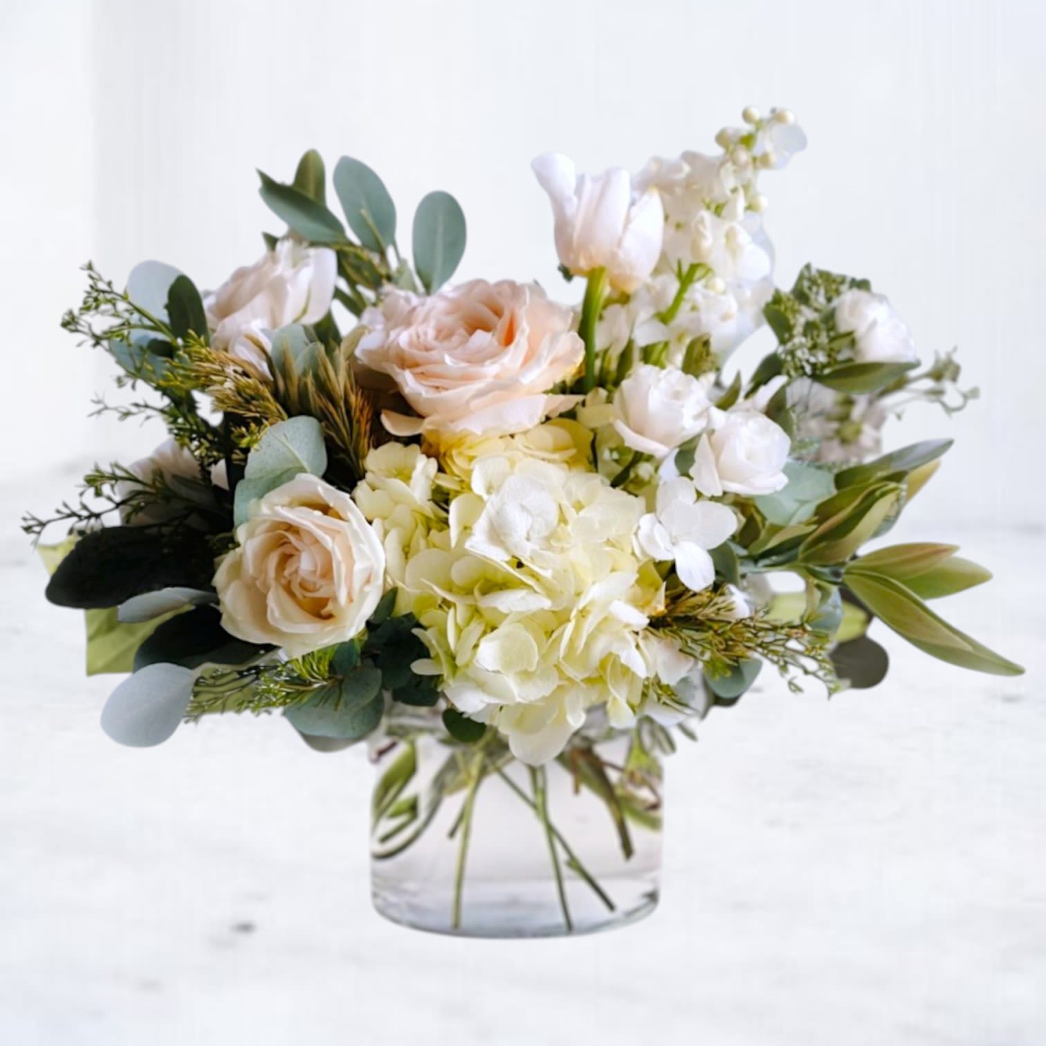 Low glass vase with white hydrangeas, peach roses, and other white flowers in a soft, airy arrangement