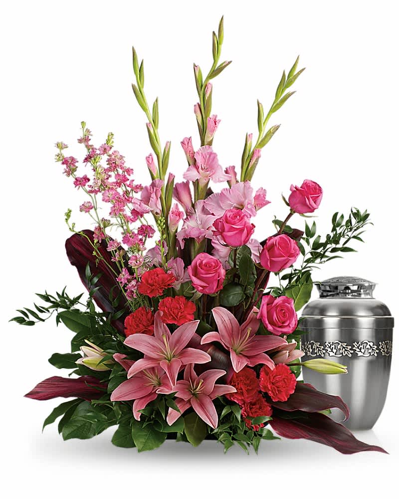 Tall pink and red floral sympathy arrangement beside a silver cremation urn