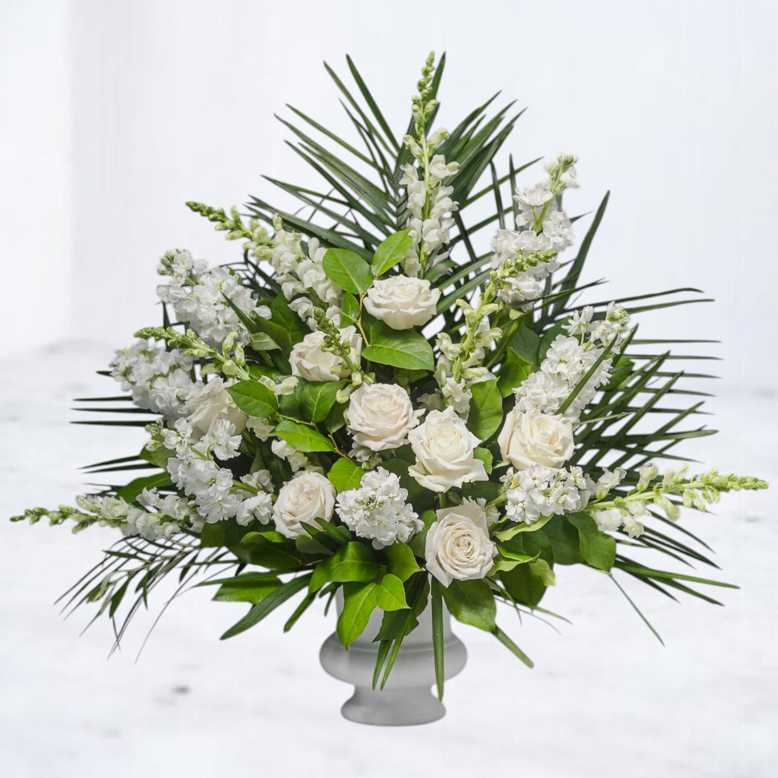 Tall white rose and snapdragon arrangement in a white pedestal vase
