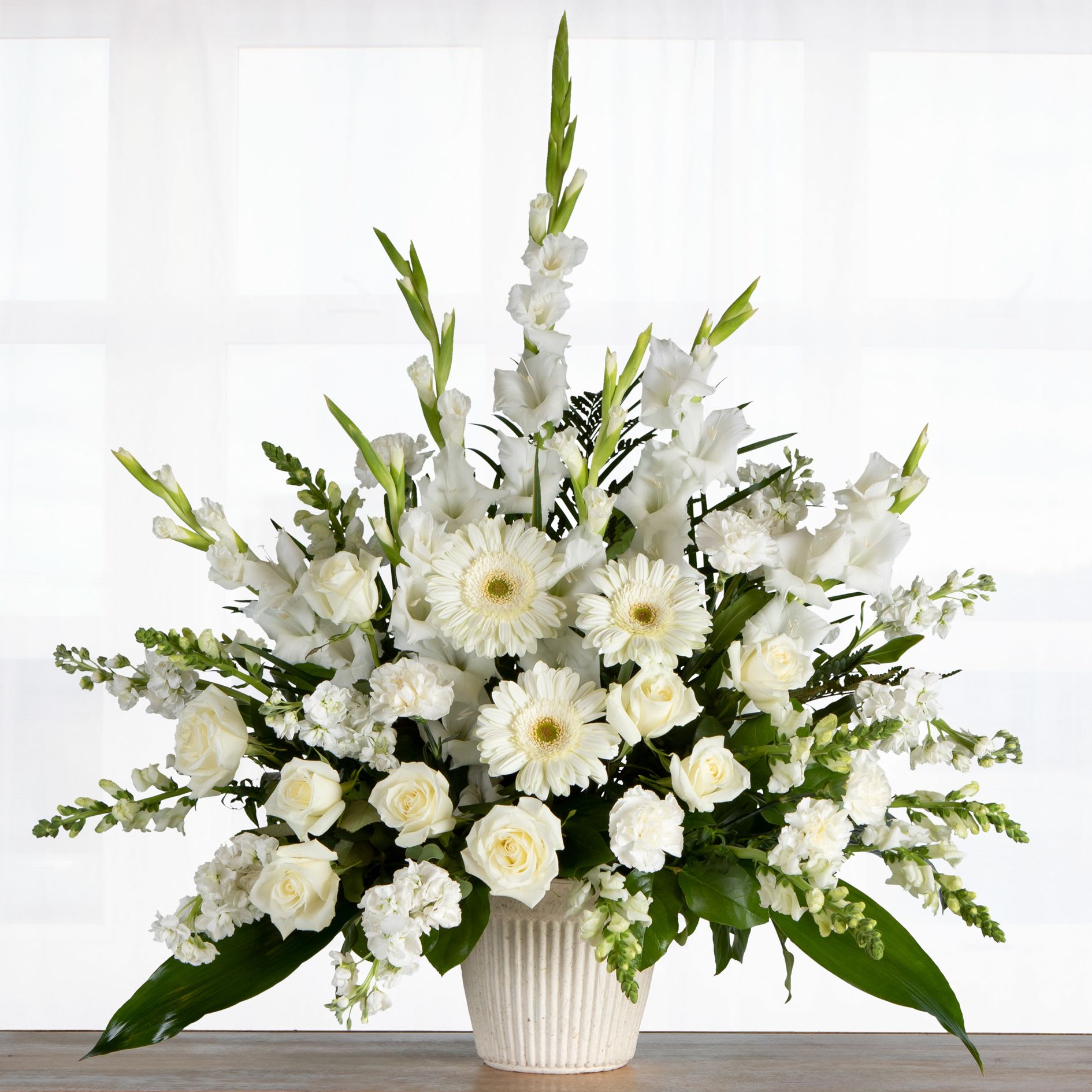 Tall white arrangement of roses, gerbera daisies, and other blooms in a ribbed white pot