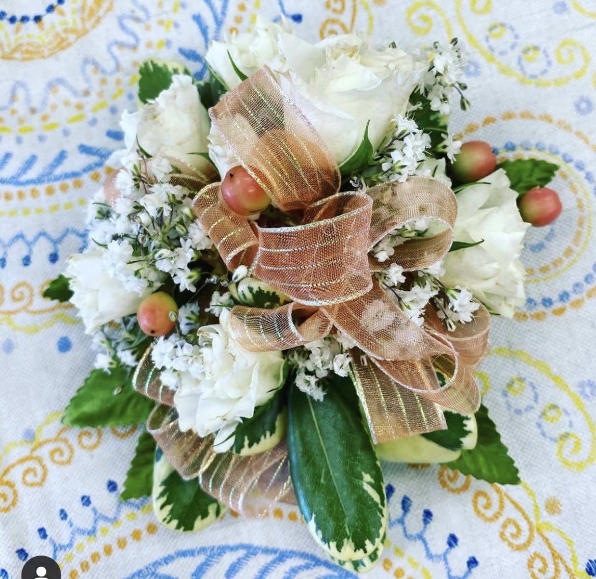 Compact white rose corsage with peach ribbon, white filler flowers, and berries on variegated foliage.