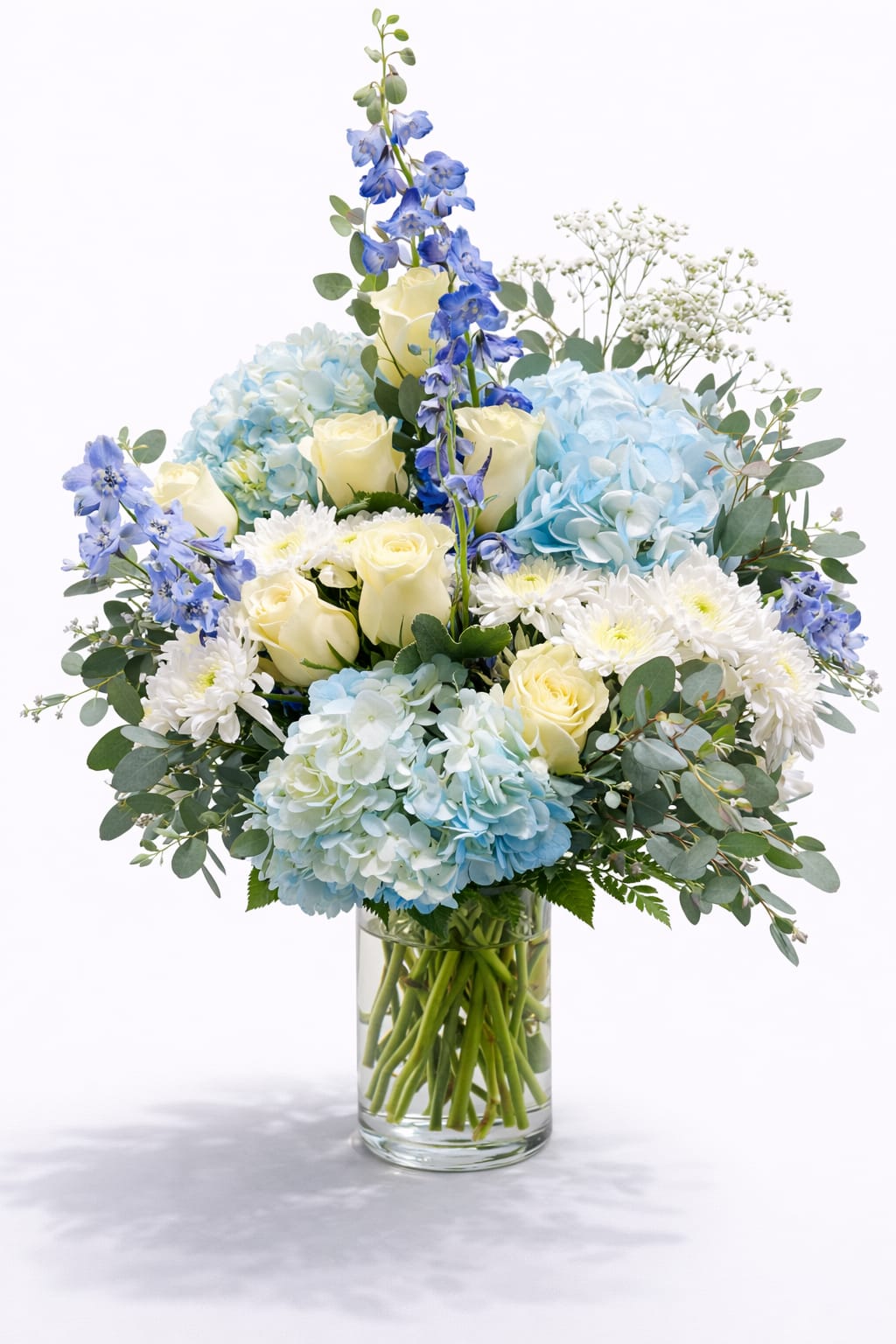 Blue hydrangeas, ivory roses and white mums in a clear glass cylinder vase