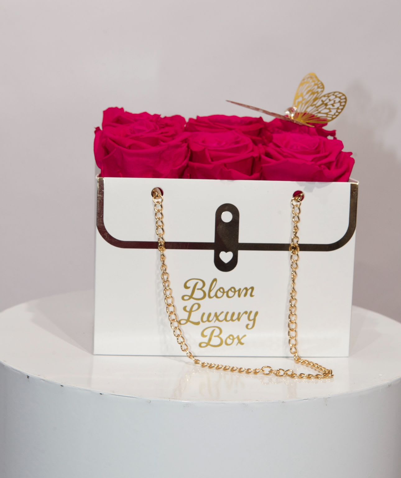 Hot pink roses arranged in a white purse-style box with gold chain and butterfly accent.