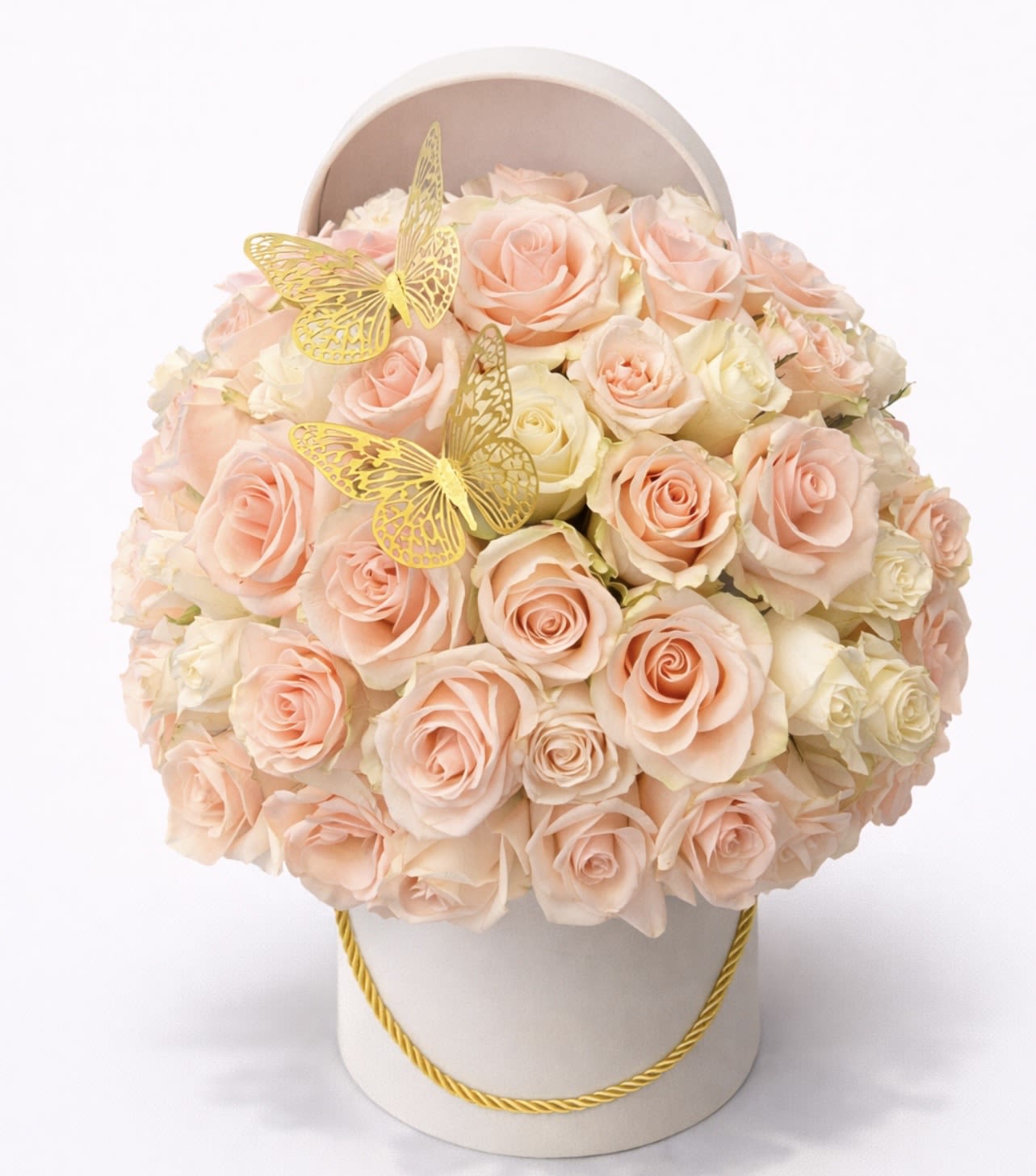Round hatbox arrangement of peach and cream roses accented with two gold butterfly decorations.