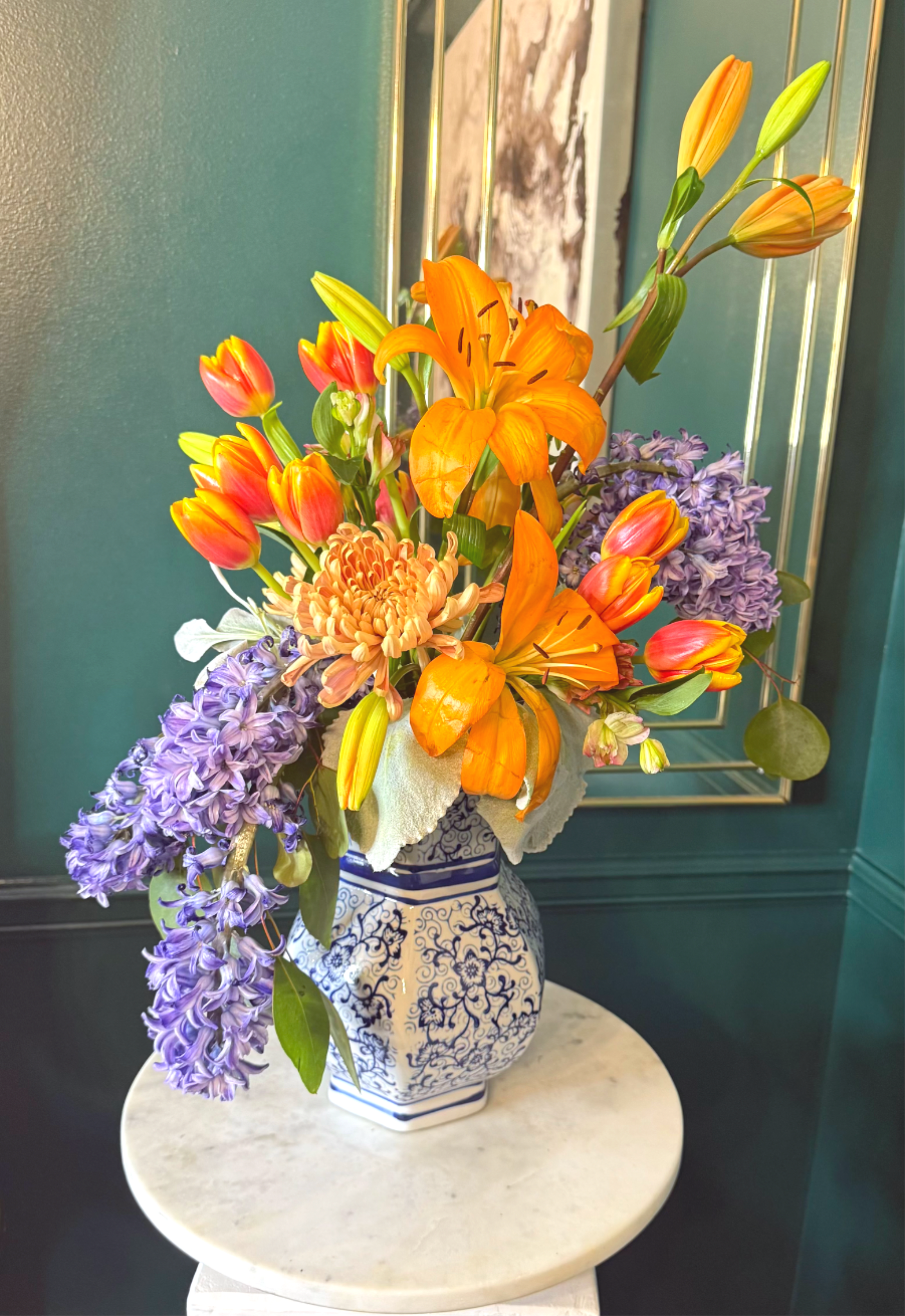 Bright orange lilies, tulips, chrysanthemum, and purple hyacinths in a blue and white ceramic vase